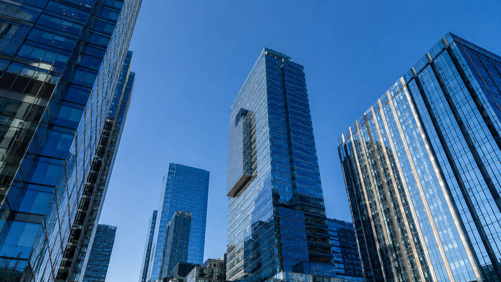 Glass office towers in a financial district photographed from street level against a clear blue sky.